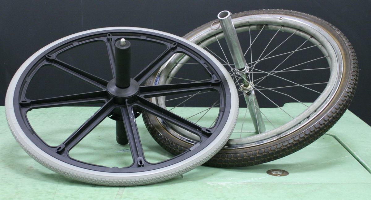 Two bicycle wheels on a green bench — one with black mag-style spokes and cylindrical axle handle, one with traditional wire spokes and extended axle