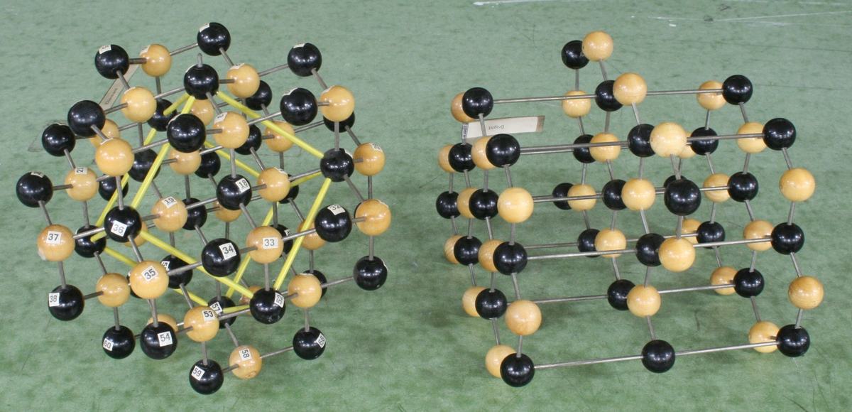 Two ball-and-stick crystal models with black and tan spheres connected by metal rods; left model has yellow-highlighted bonds showing tetrahedral coordination, right model shows a layered structure