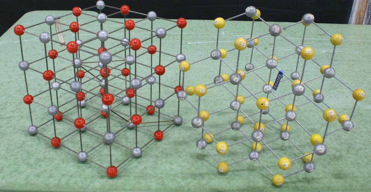 Two larger ball-and-stick crystal models: left has gray and red spheres in a cubic ionic arrangement, right has gray and yellow spheres in a tetrahedral bonding structure