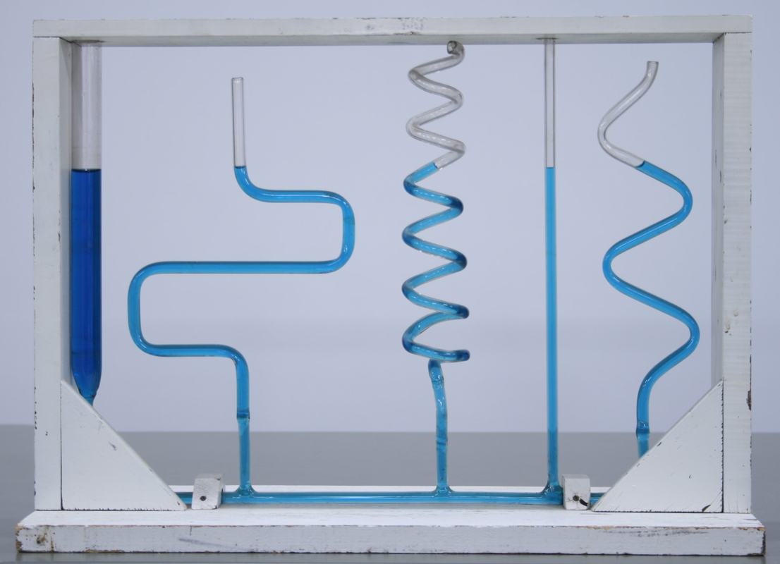 Fluid level tube apparatus in a white frame: four connected glass tubes filled with blue-colored water -- one straight wide tube, one with zigzag bends, one spiral, and one S-curve -- all showing water at the same height