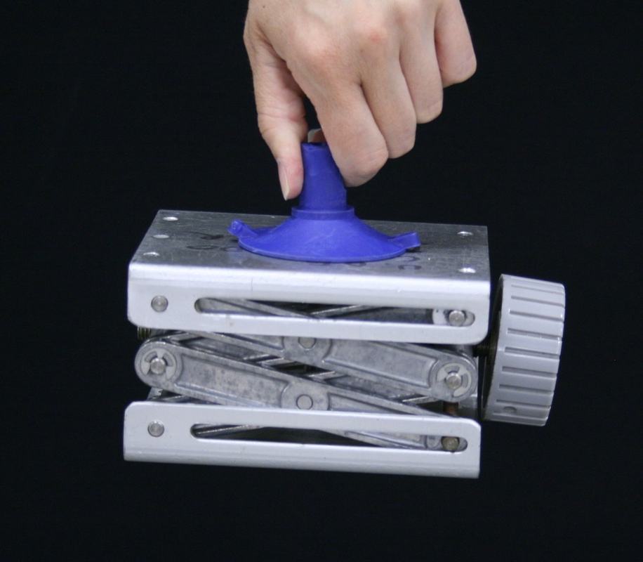 Hand lifting the lab jack by the suction cup handle, with the jack suspended in mid-air against a black background