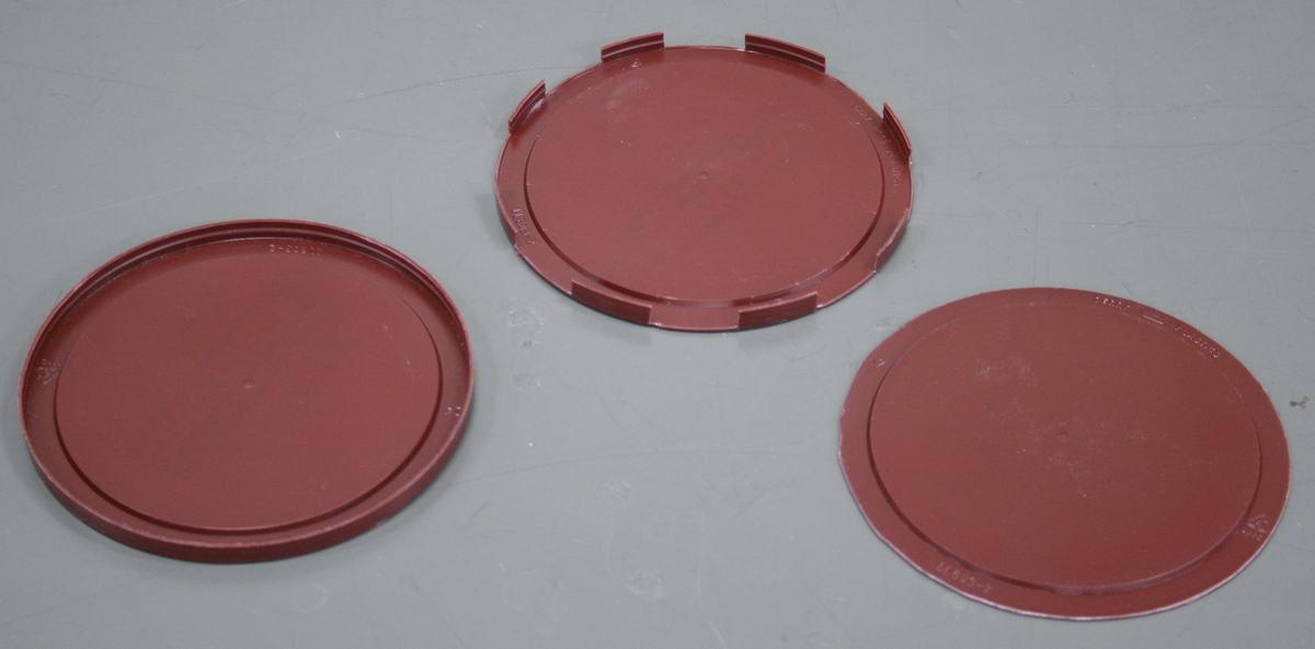 Three dark red plastic coffee can lids on a white surface: left has intact rim, center has partial rim with tab cutouts, right has rim fully removed
