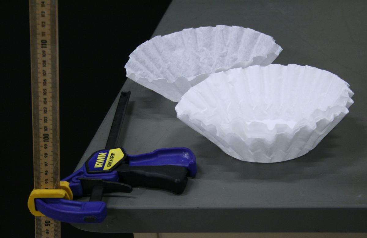 Two white basket-style coffee filters, an Irwin Quick-Grip bar clamp, and the bottom of a two-meter stick on a gray table