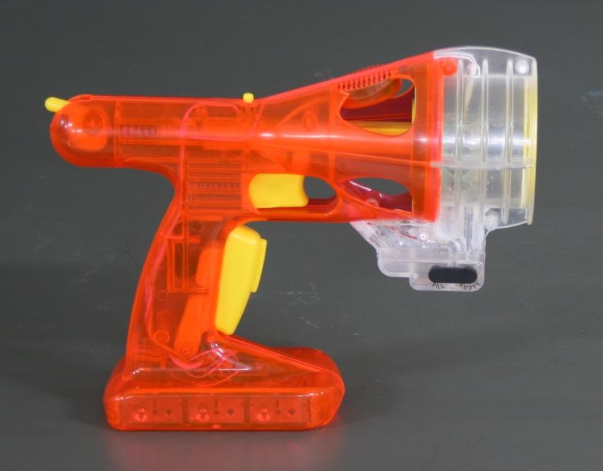 Side view of the Zero Blaster: a translucent red and yellow plastic toy with a clear cylindrical smoke chamber at the front
