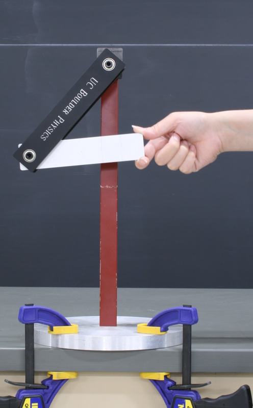 Hand holding the silver lower bar in a "4" shape against the red support column, demonstrating the out-of-phase initial condition