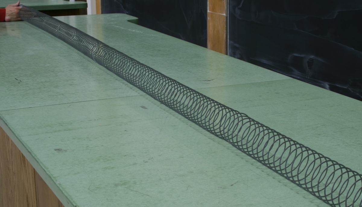 Large metal Slinky stretched along a green lecture bench, viewed from bench level