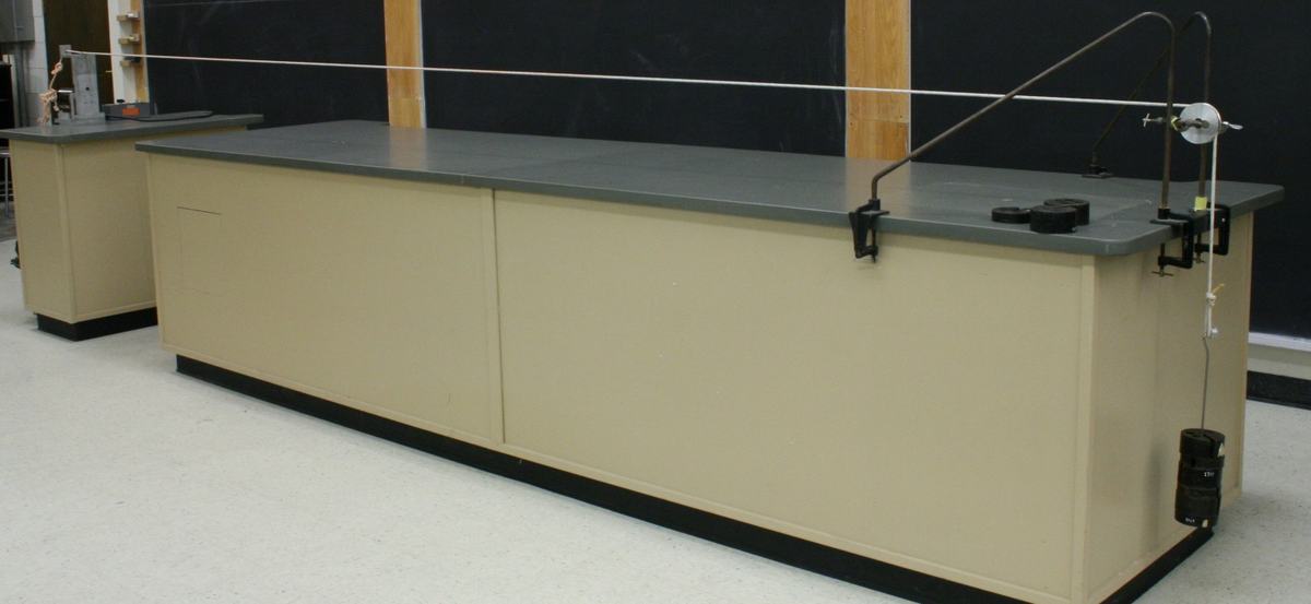 Rope stretched across the full length of the lecture bench, with motor driver at the far left end and pulley assembly with hanging mass at the right end