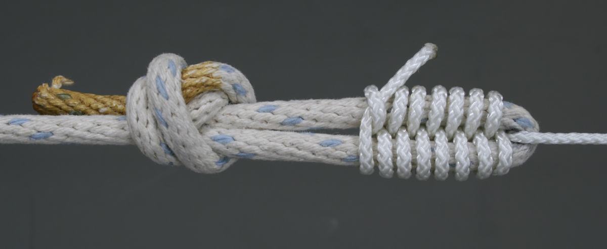 Close-up of the rope junction: a thick white braided rope with blue flecks joined to a thinner white cord via a racking knot on the left, with tight coil wrapping securing the connection on the right