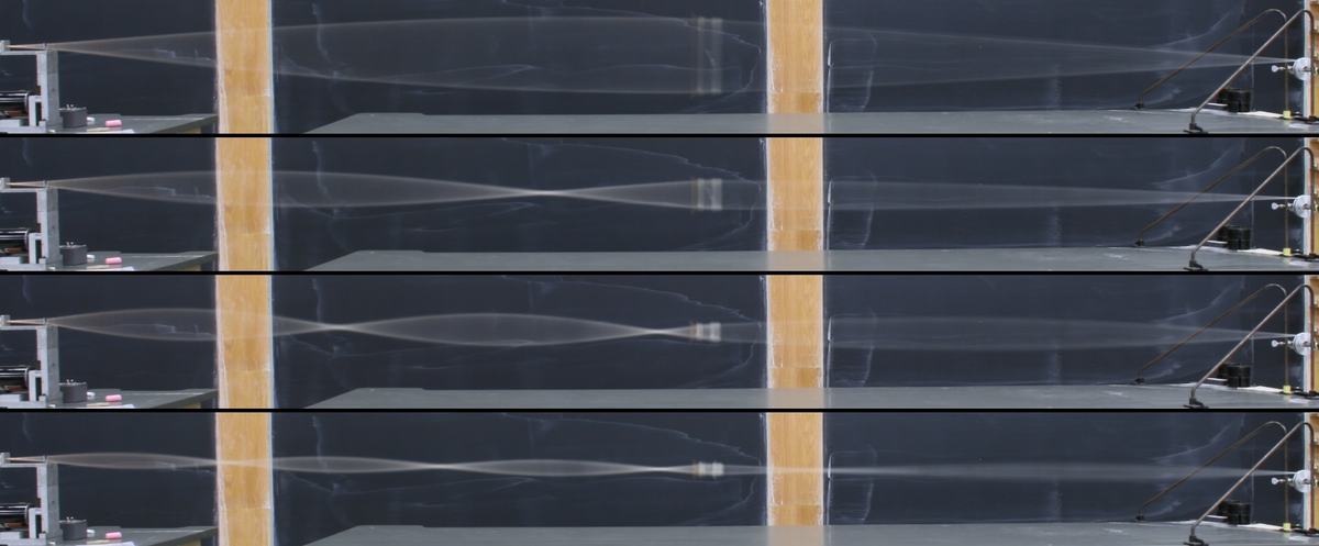 Composite of four photos showing standing waves at successive harmonics in a nonuniform rope stretched across a lecture bench, with the motor driver on the left and pulley assembly on the right