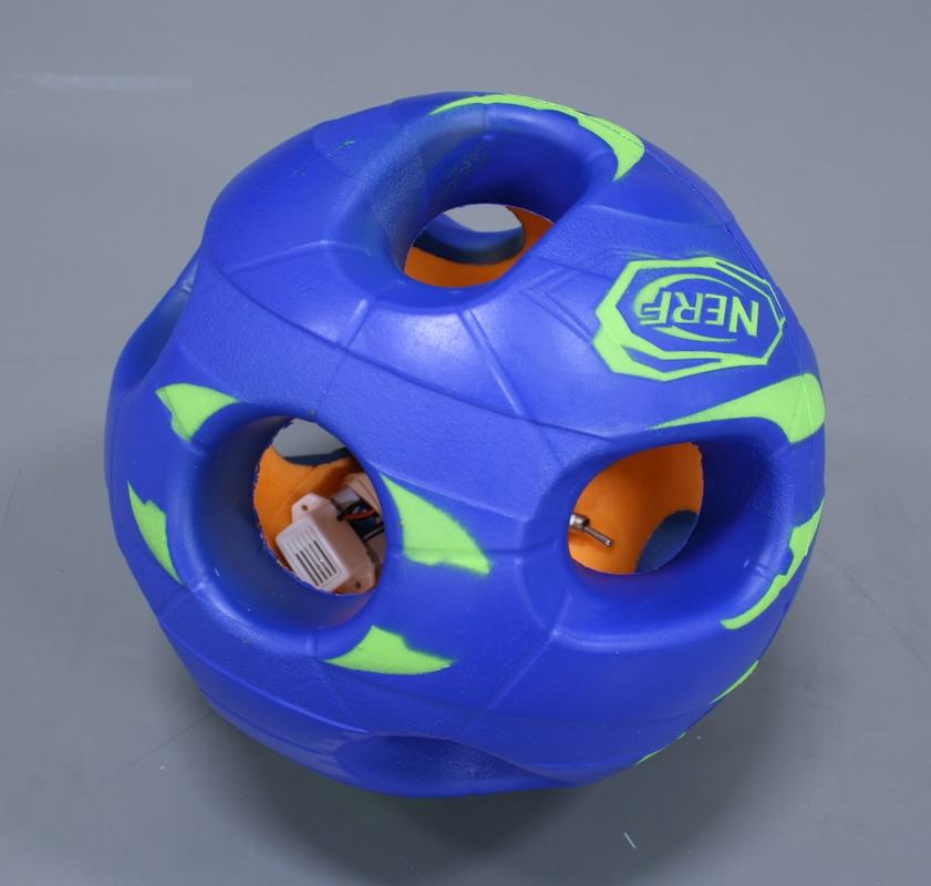 Blue and green hollow Nerf ball with circular openings; a battery-powered buzzer circuit is visible inside through the holes