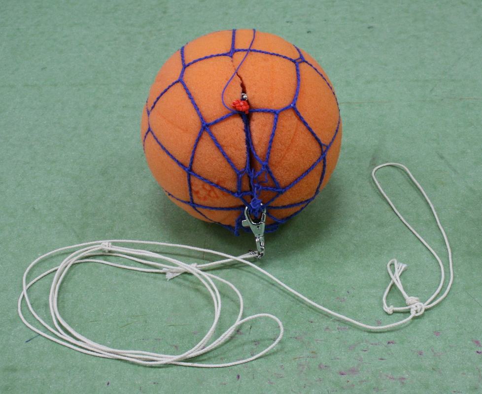 Orange foam ball wrapped in blue netting with attached clip and white string coiled on green surface, containing internal buzzer for Doppler effect demonstration