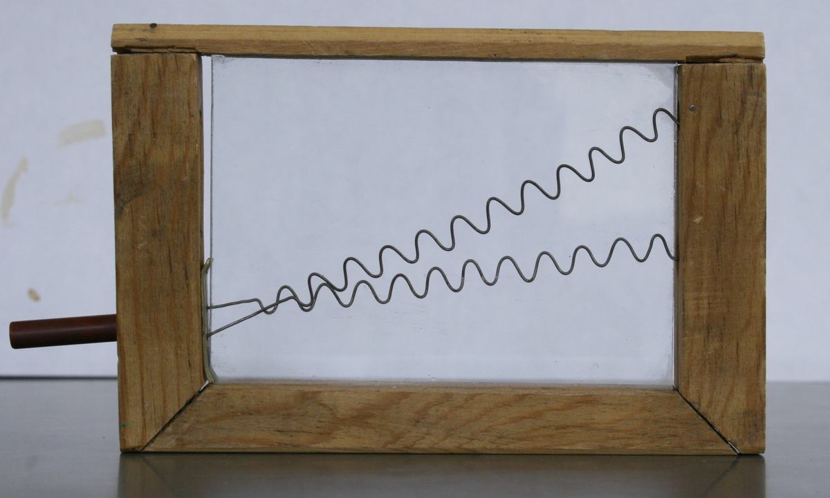 Same wooden-framed box with the two sinusoidal wire patterns shifted so their peaks and troughs align in phase. Handle on left is in a different position.