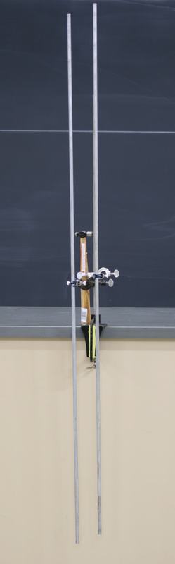 Two aluminum rods mounted vertically in finger clamps on right-angle clamps attached to a bench clamp rod at a table edge, with a small hammer resting in the assembly