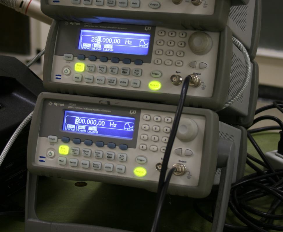 Two Agilent function generators stacked vertically, LCD displays showing frequencies of approximately 299 Hz and 300 Hz