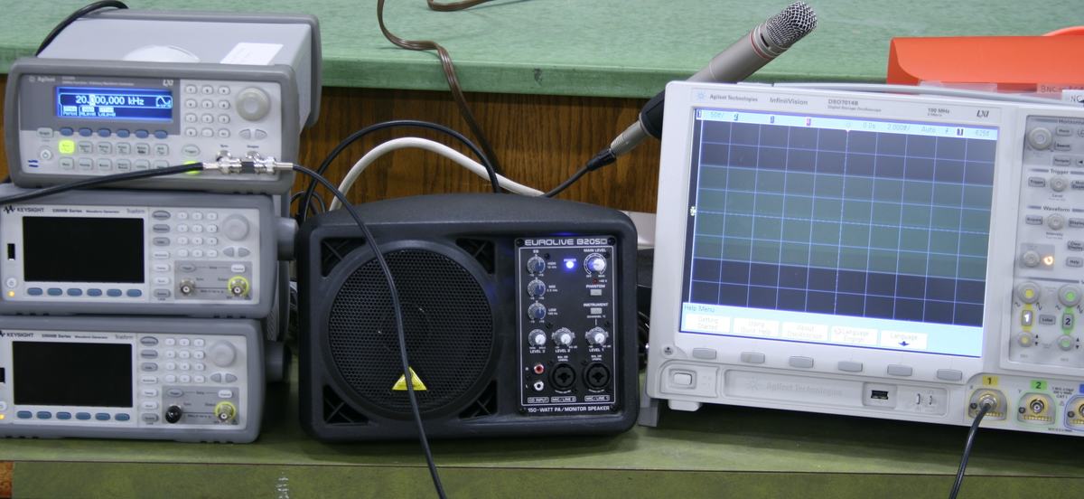 Two signal generators, a Behringer Eurolive B205D powered monitor speaker, an Agilent oscilloscope, and a microphone on a lab bench