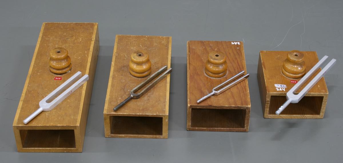 Four wooden resonance boxes of decreasing size arranged in a row, each with a turned wooden coupling knob on top and an open front face. A tuning fork rests on each box.