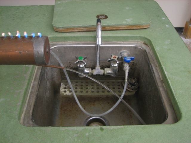 Far end of the Ruben's tube extending over a lecture bench sink, with clear tubing connecting the copper cooling drain tube to the water faucet