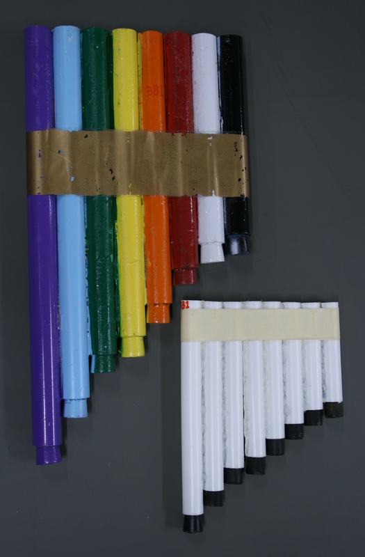 Two homemade PVC panpipe sets: one rainbow-colored with gold tape binding, one white with black endcaps and masking tape binding
