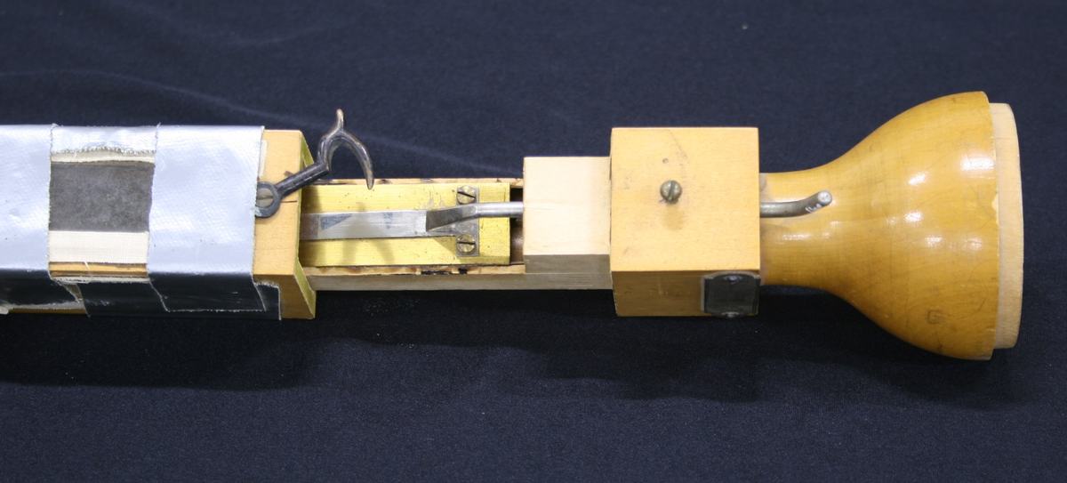 Close-up of reed mechanism near the bell end: metal reed strip mounted between wooden blocks, with a lever arm and wing nut for pitch control