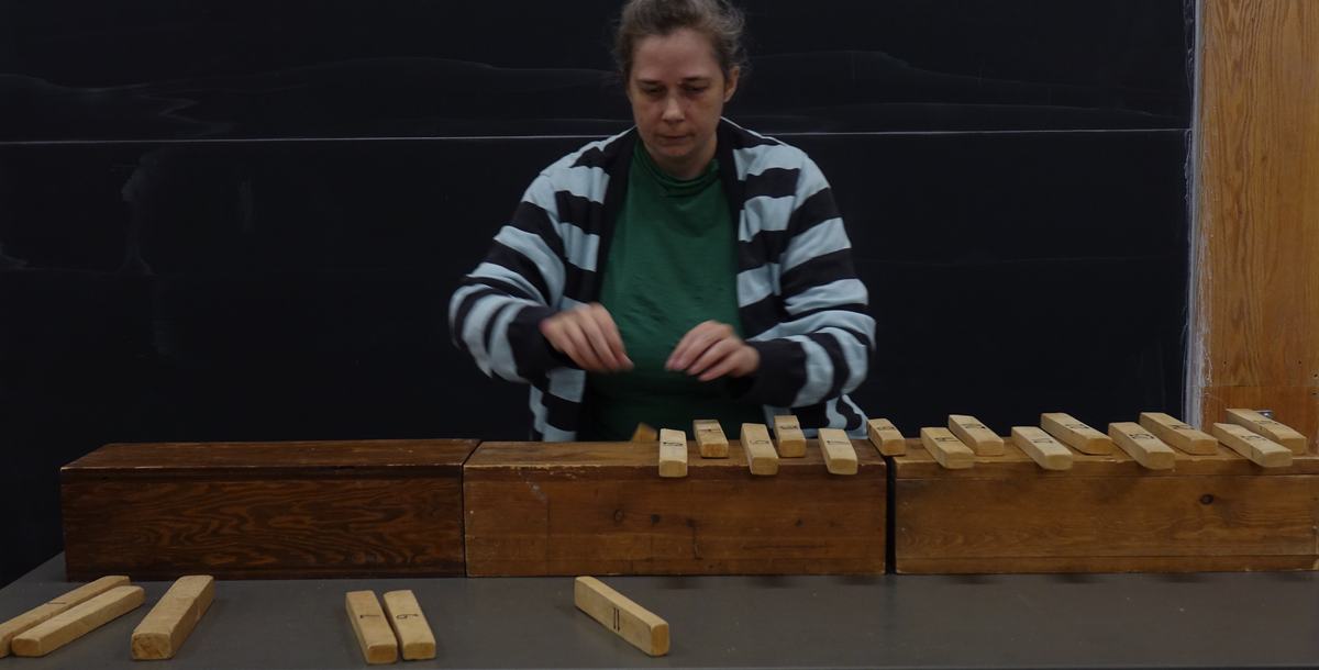 Person arranging numbered wooden bars across three large wooden support blocks on a lecture table