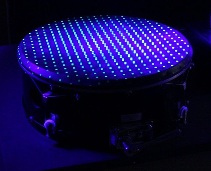 Close-up of fluorescent drum membrane under UV showing a standing wave pattern with diagonal stripe-like nodal structure