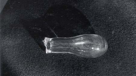 Clear glass Bologna bottle with thick rounded bulb and narrow neck, resting on dark surface