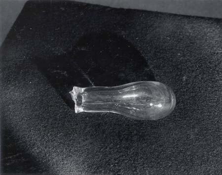 Clear glass Bologna bottle with thick rounded bulb and narrow neck, resting on dark surface