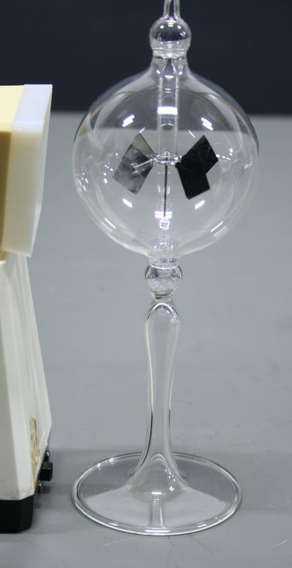 Crookes radiometer at rest: a clear glass bulb on an elegant glass stem and base, with four vanes (black on one side, silver on the other) visible inside