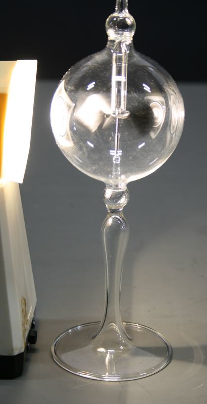 Crookes radiometer with a light source illuminating it from the left; the vanes are spinning (motion blur visible)