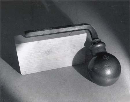 Cast iron ice bomb: a spherical vessel with a threaded cap connected by a curved pipe to a rectangular metal block, shown before freezing