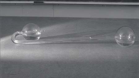 Cryophorus: a glass apparatus with two spherical bulbs connected by a long glass tube, lying on a tabletop in front of a chalkboard
