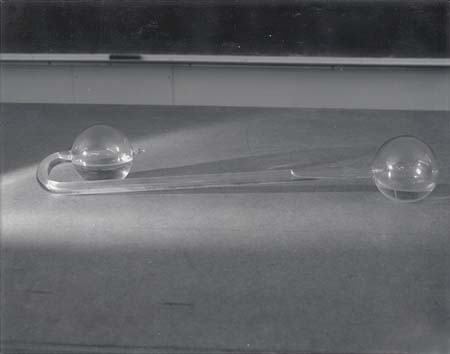 Cryophorus: a glass apparatus with two spherical bulbs connected by a long glass tube, lying on a tabletop in front of a chalkboard