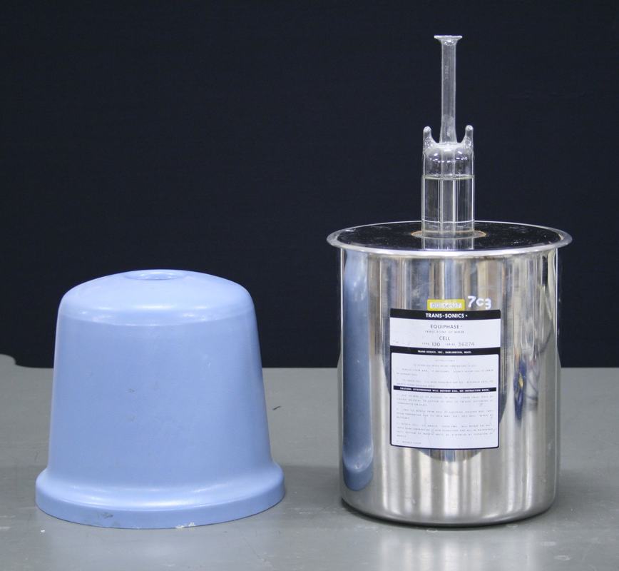 Trans-Sonics Equiphase triple point cell: polished stainless steel cylinder with glass reentrant thermometer well protruding from the top, and blue plastic protective cap shown beside it
