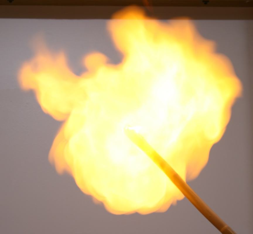 Bright yellow-orange fireball from an ignited hydrogen balloon, with the candle stick visible entering from the lower right
