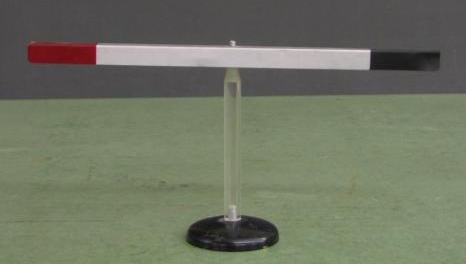 Bar electroscope (versorium): lightweight aluminum vane with red and black painted ends, balanced on a clear plastic pivot post on a round black base