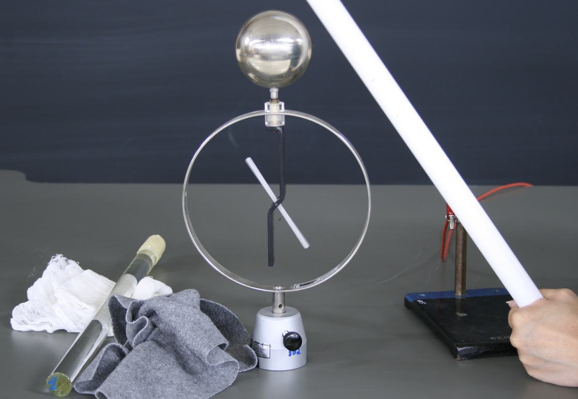 Electroscope with deflected needle as charged white Teflon rod is held near the metal sphere from the right