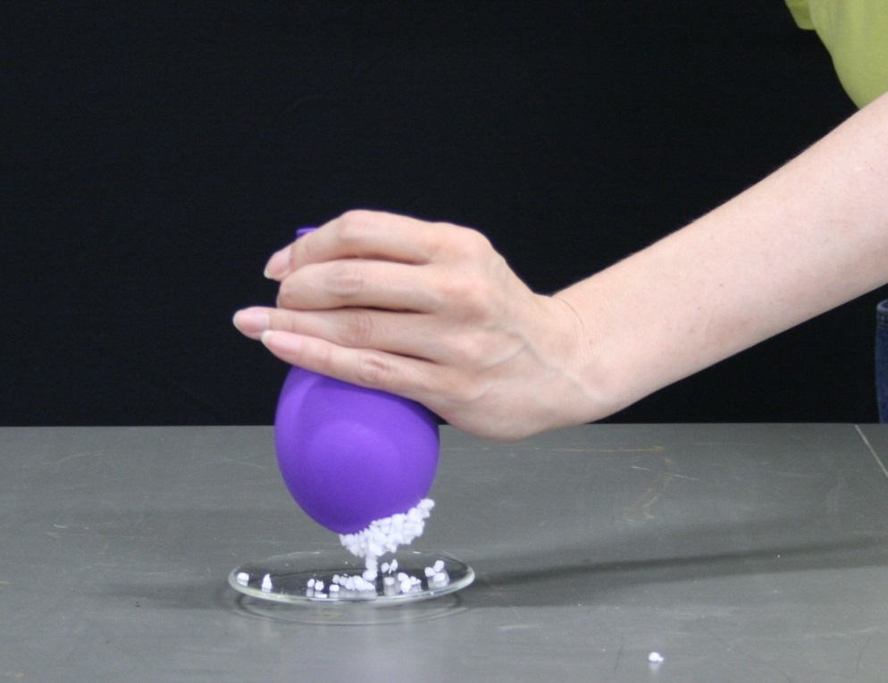 Partially deflated purple balloon with many foam confetti pieces clinging to its surface, held above watch glass