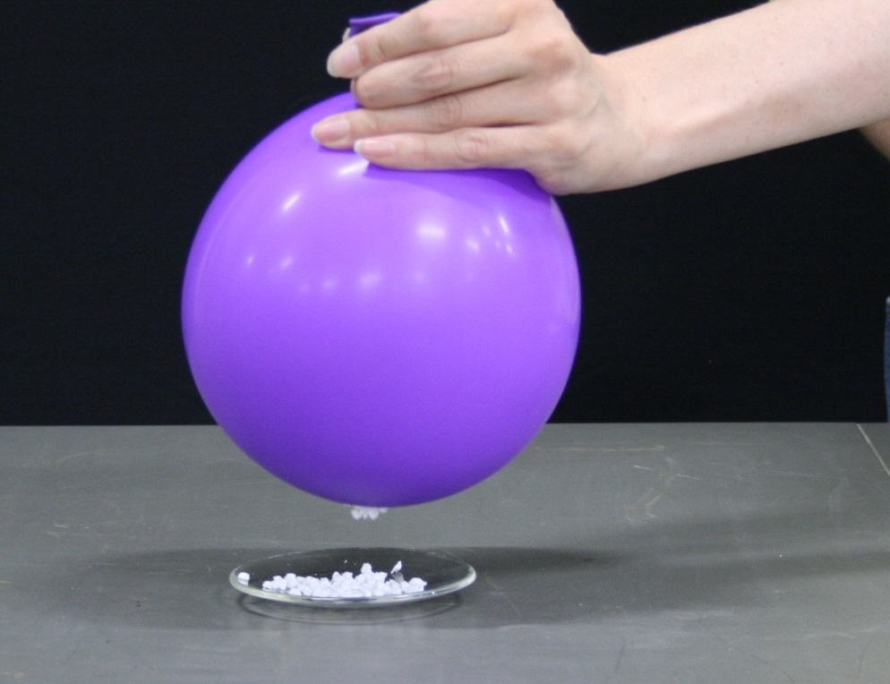 Charged purple balloon held above watch glass; a few foam confetti pieces jumping toward the balloon