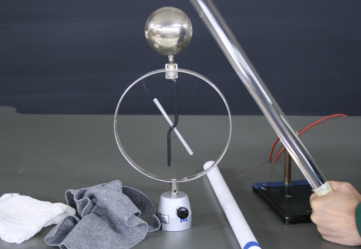 Electroscope with deflected needle, clear acrylic rod held near the sphere from upper right