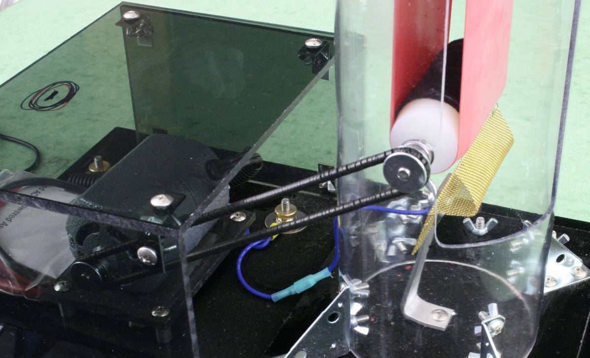 Close-up of lower section showing motor, gold fabric belt on rollers, lower discharge comb, and wiring on a black base with clear plastic shielding