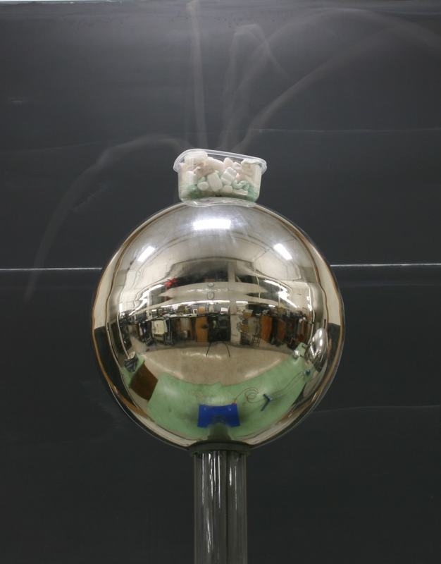 Small clear plastic container filled with foam packing peanuts sitting on top of the Van de Graaff generator dome