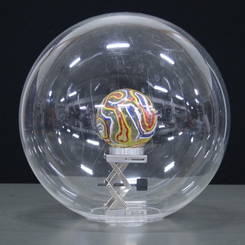 Clear acrylic sphere with a colorful swirled marble at the center, supported by a small scissor-jack stand inside the sphere