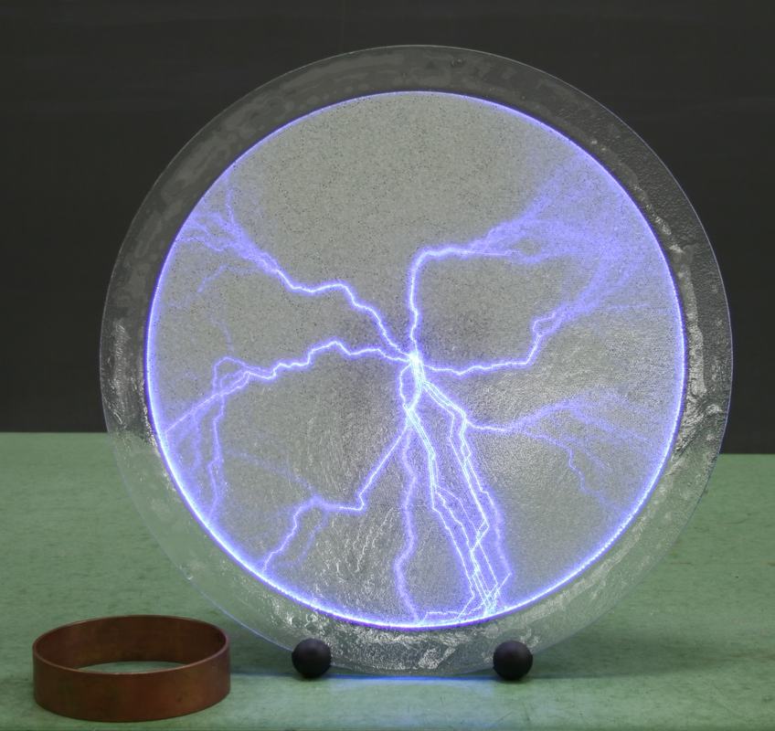 Plasma disk without the metal ring, showing discharge paths spreading freely across the entire disk surface; the copper ring sits on the table beside the disk