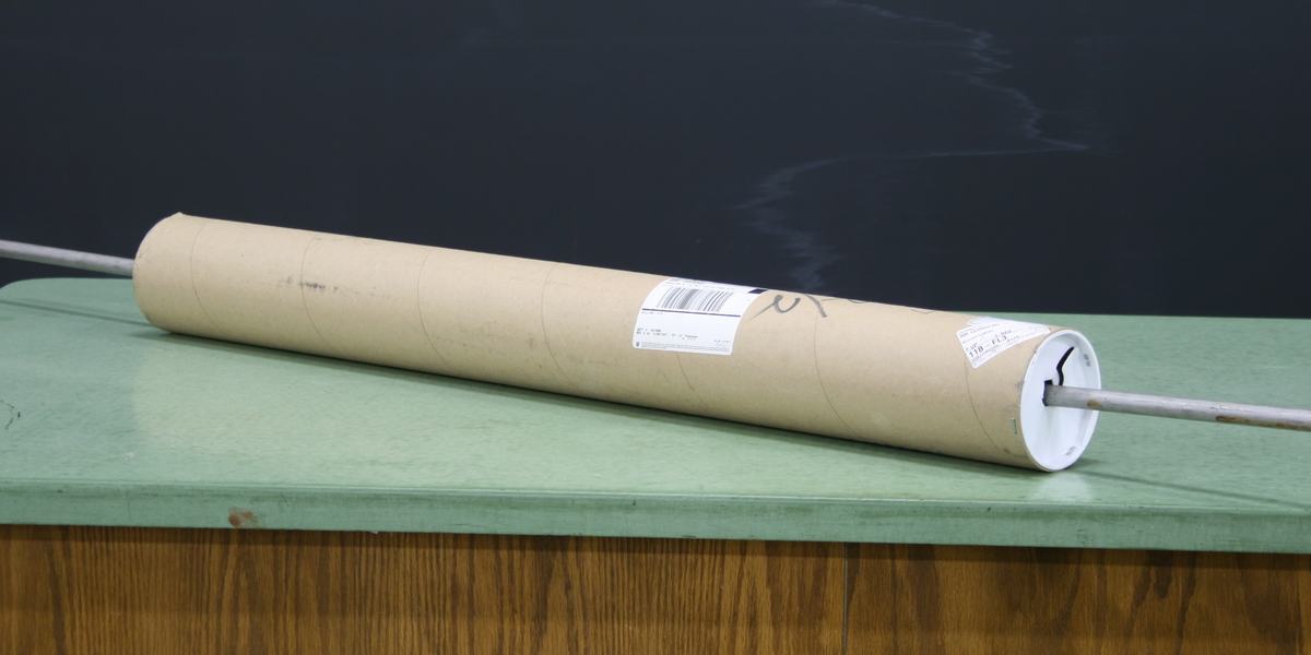 Cardboard mailing tube with white plastic end caps and a metal rod passing through the center axis, lying on a green lab bench