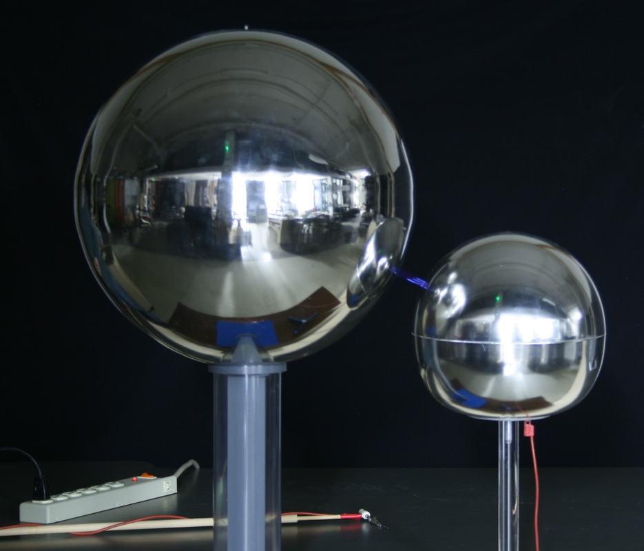 Closer view of Van de Graaff dome and grounded sphere with a spark visible between them, red grounding wire connected at base