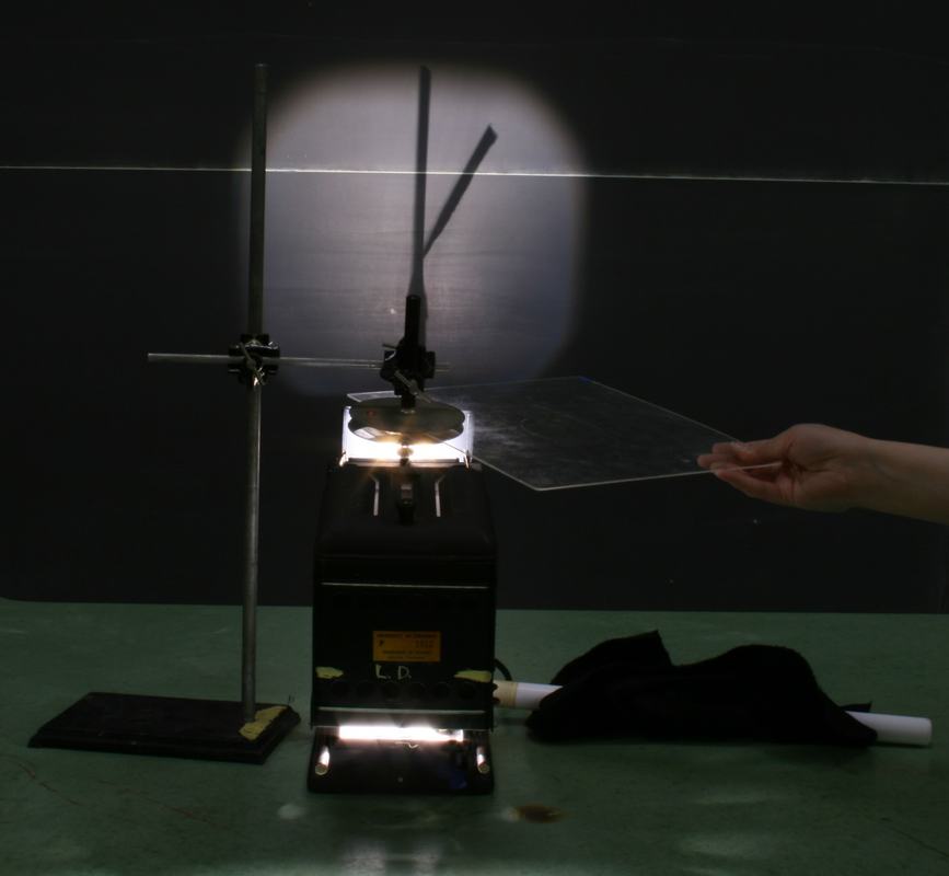 Hand inserting transparent plastic dielectric sheet between the capacitor plates while electroscope projects leaf deflection on board