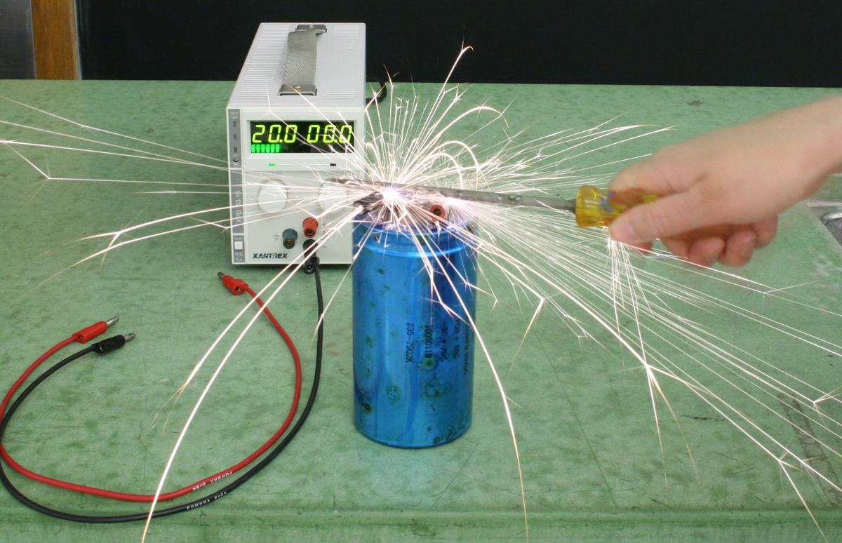 Brilliant white sparks radiating from the capacitor terminals as a hand bridges them with the screwdriver