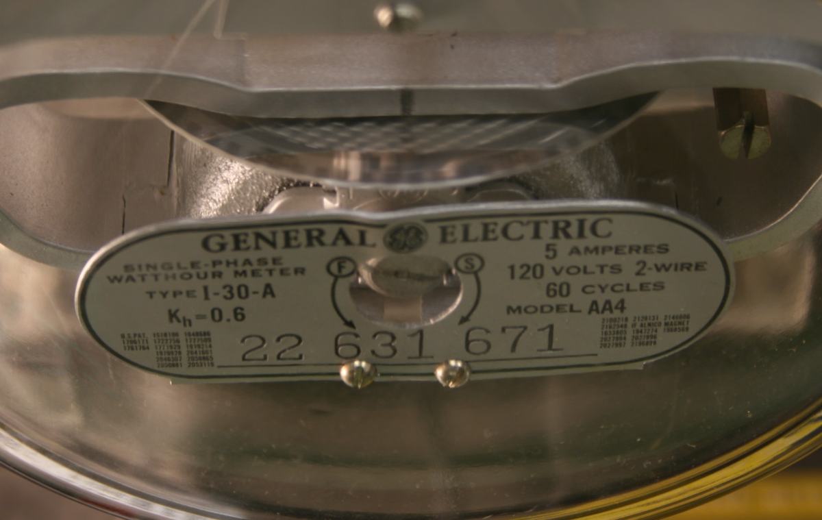 Close-up of GE watthour meter nameplate showing Type I-30-A, Kh=0.6, 5 amperes, 120 volts 2-wire, 60 cycles, with visible disc blur from the 40W incandescent load