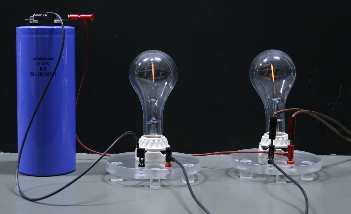 Both bulbs show faint, nearly identical glowing filaments as the capacitor discharges through the circuit