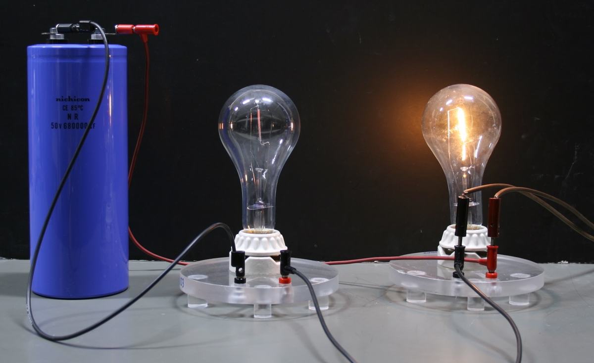 Same setup; the left bulb near the capacitor is completely dark while the right bulb remains brightly lit